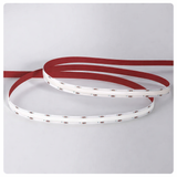 Unlit Seamless RGB LED strip with white circuit board and red backing liner, shown in loose coils